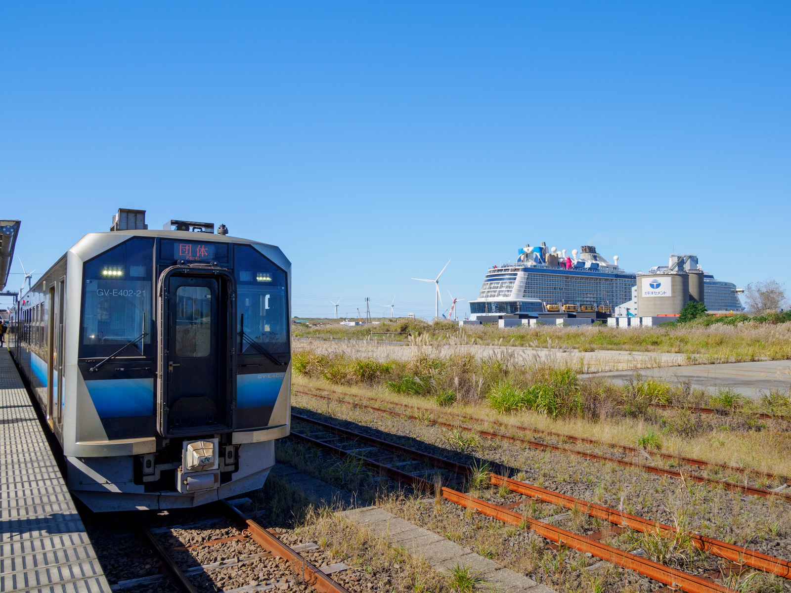 秋田港駅に停車する秋田港クルーズ列車と、秋田港に停泊するクルーズ船「クアンタム・オブ・ザ・シーズ」(2024年10月)