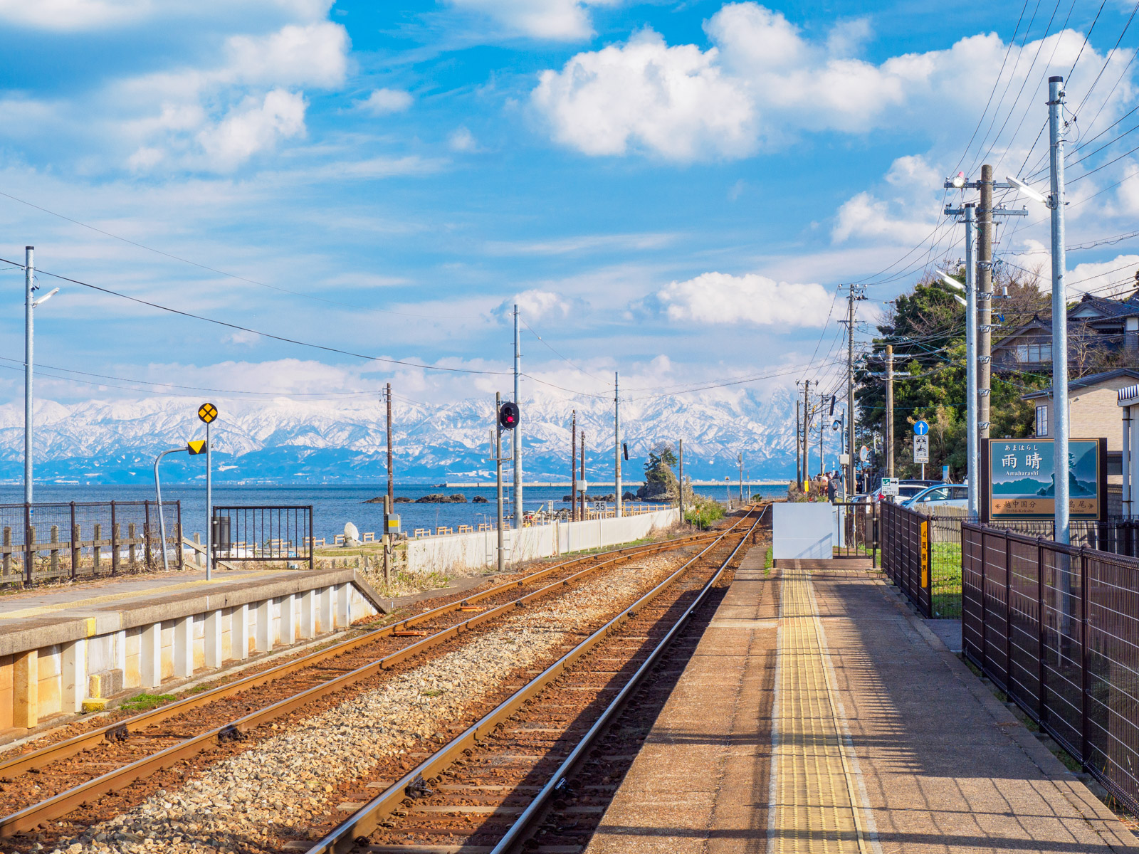 雨晴駅のホームから見た、線路越しの富山湾と女岩、立山連峰（2023年2月）