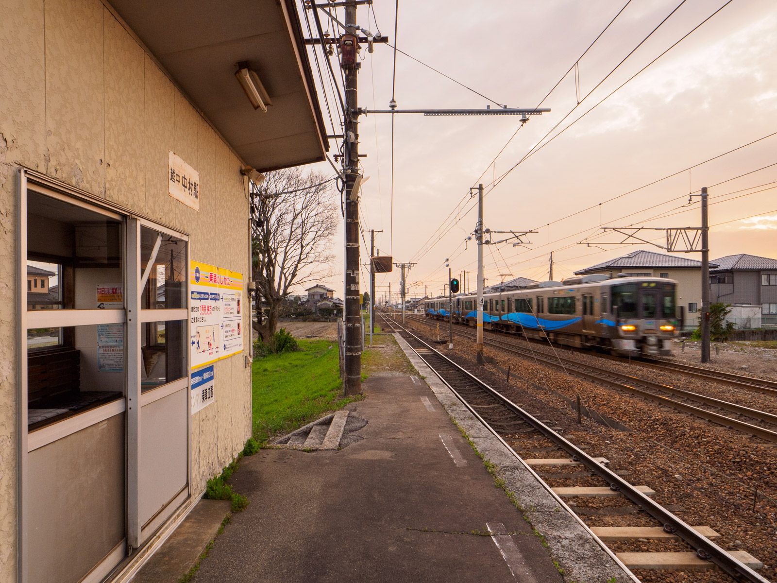 越中中村駅の待合室と、隣を通過するあいの風とやま鉄道の列車（2024年4月）