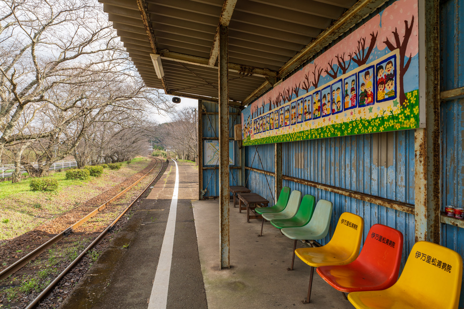 浦ノ崎駅の上屋と色とりどりのベンチ、開花前の桜並木(2026年3月)
