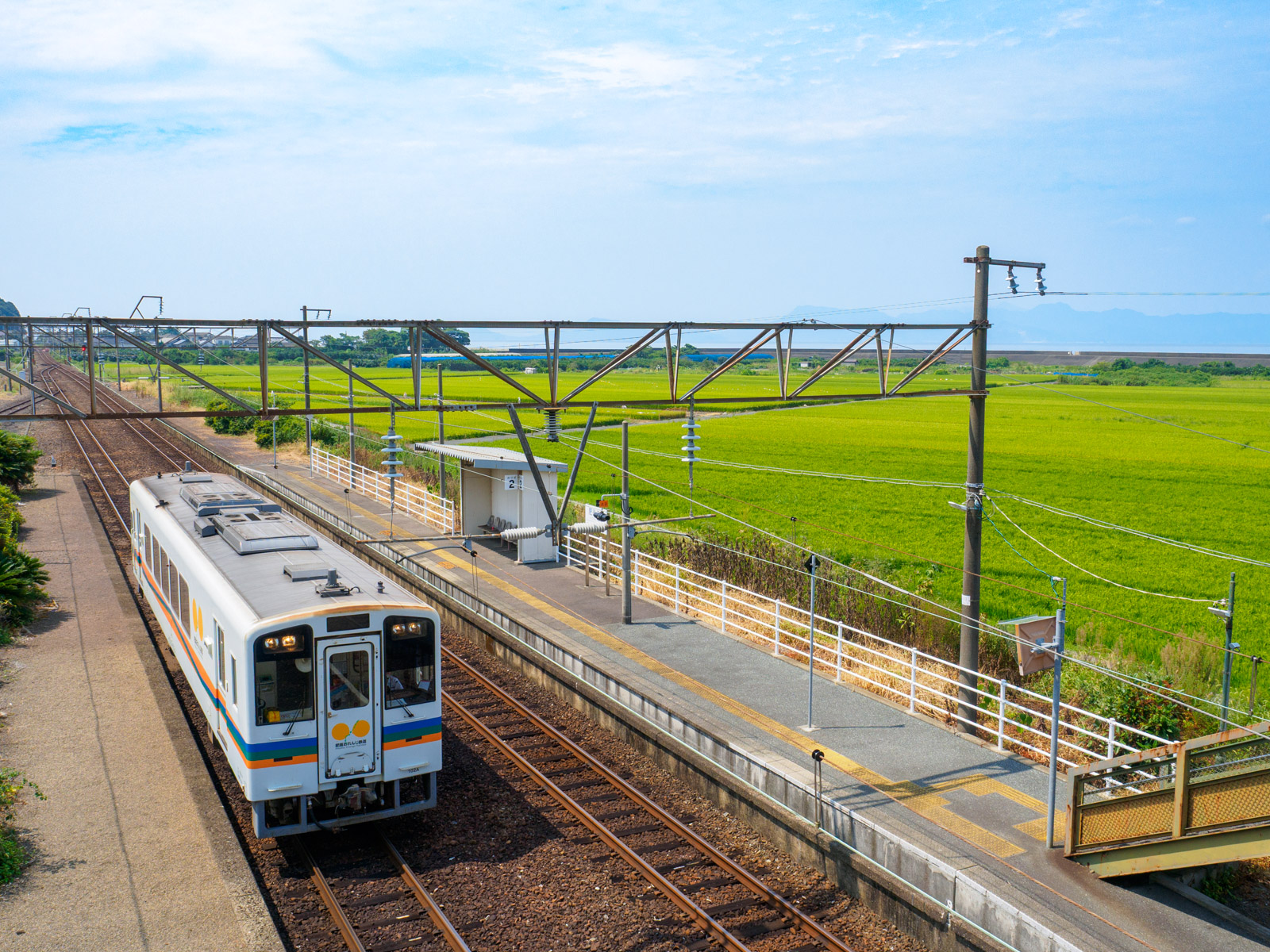 肥後二見駅の跨線橋から見た、八代海と田んぼ、到着した列車（2016年9月）