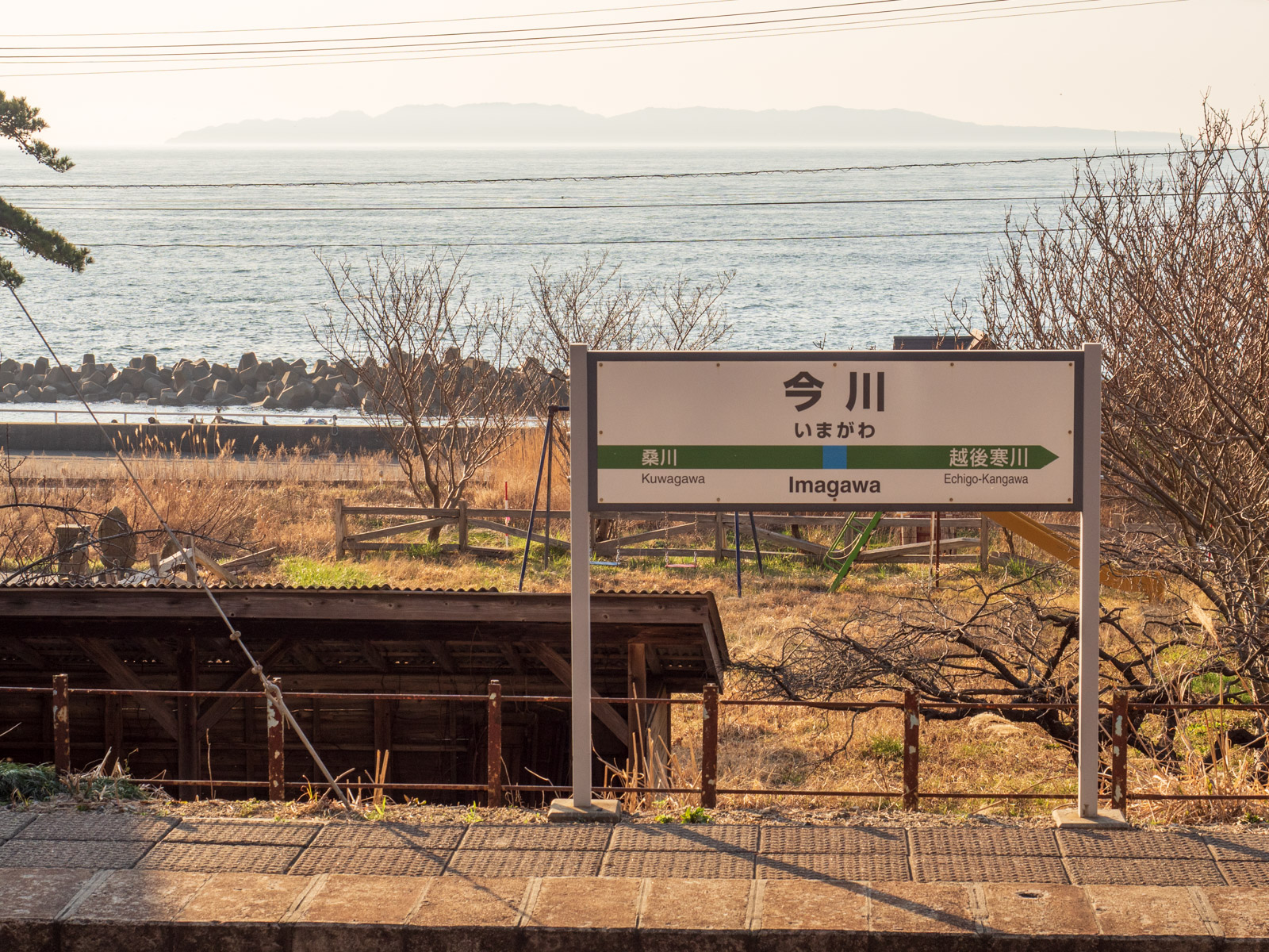 今川駅の駅名標と、夕暮れの日本海と粟島(2016年3月)