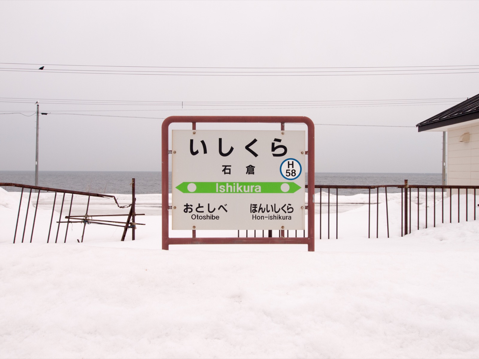 雪に埋もれた石倉駅の駅名標と、噴火湾（内浦湾）