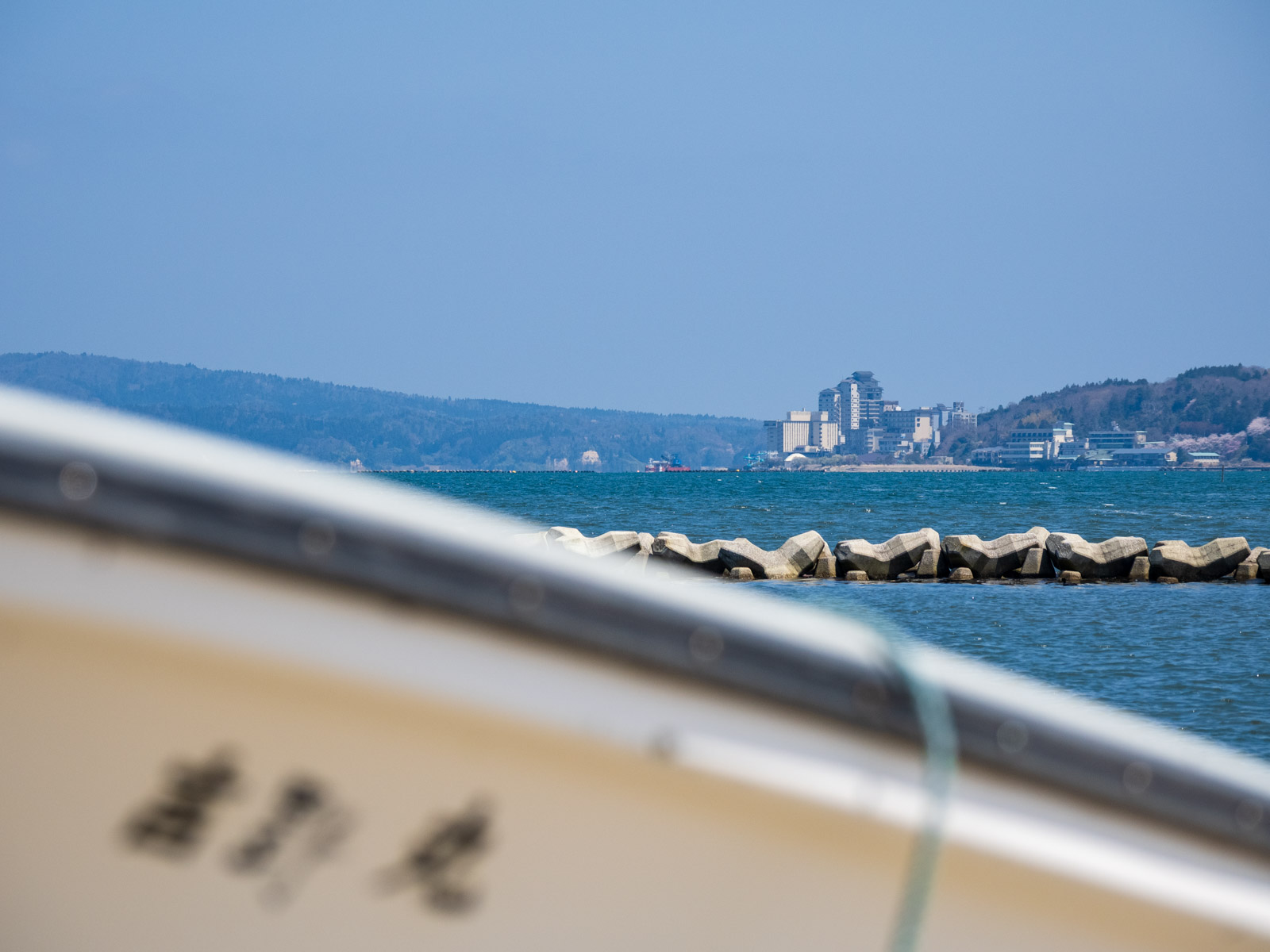 笠師保駅近くの海岸で、船越しに見た和倉温泉の温泉街(2025年4月)