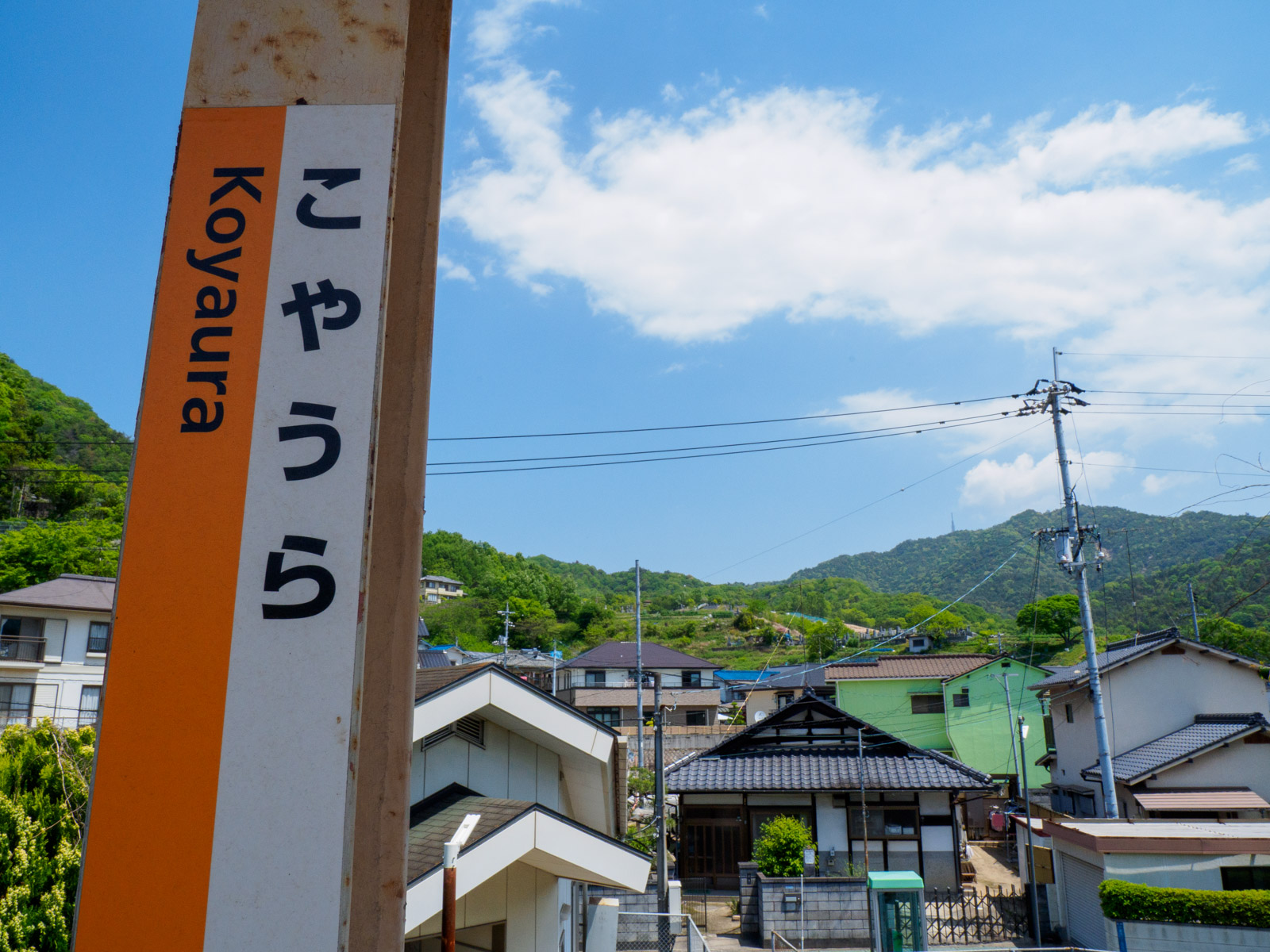 小屋浦駅の駅名標と山側の集落（2023年5月）