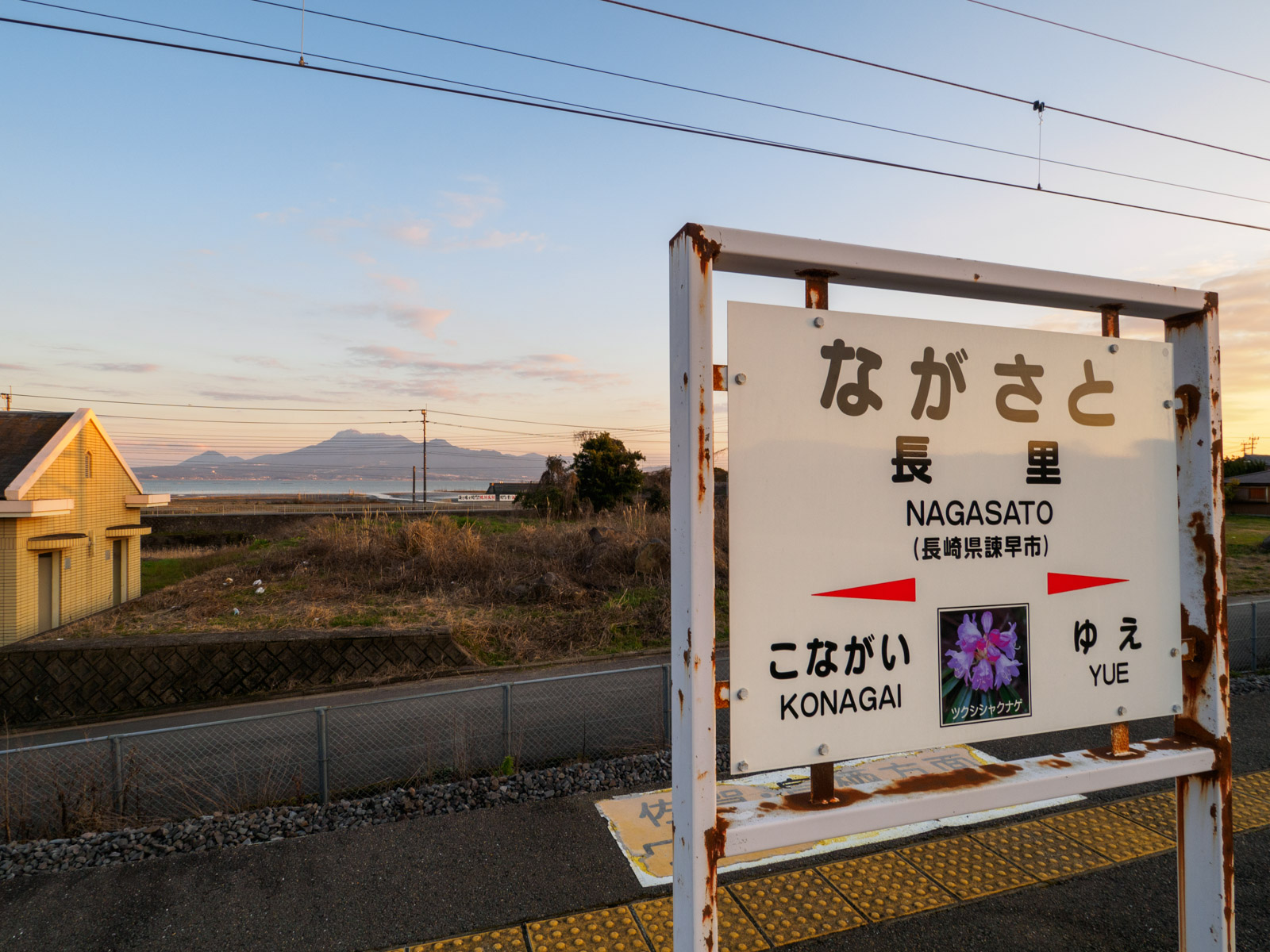 長里駅の駅名標と、ホームから見た夕暮れの諫早湾と雲仙岳（2016年2月）