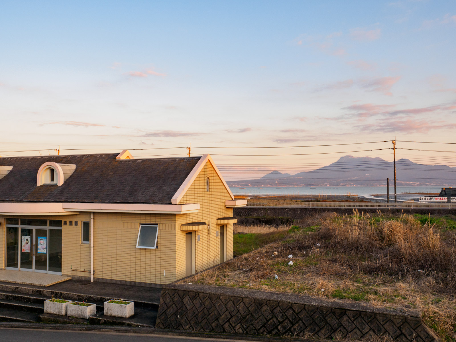 長里駅のホームから見た駅舎と、夕暮れの諫早湾と雲仙岳（2016年2月）