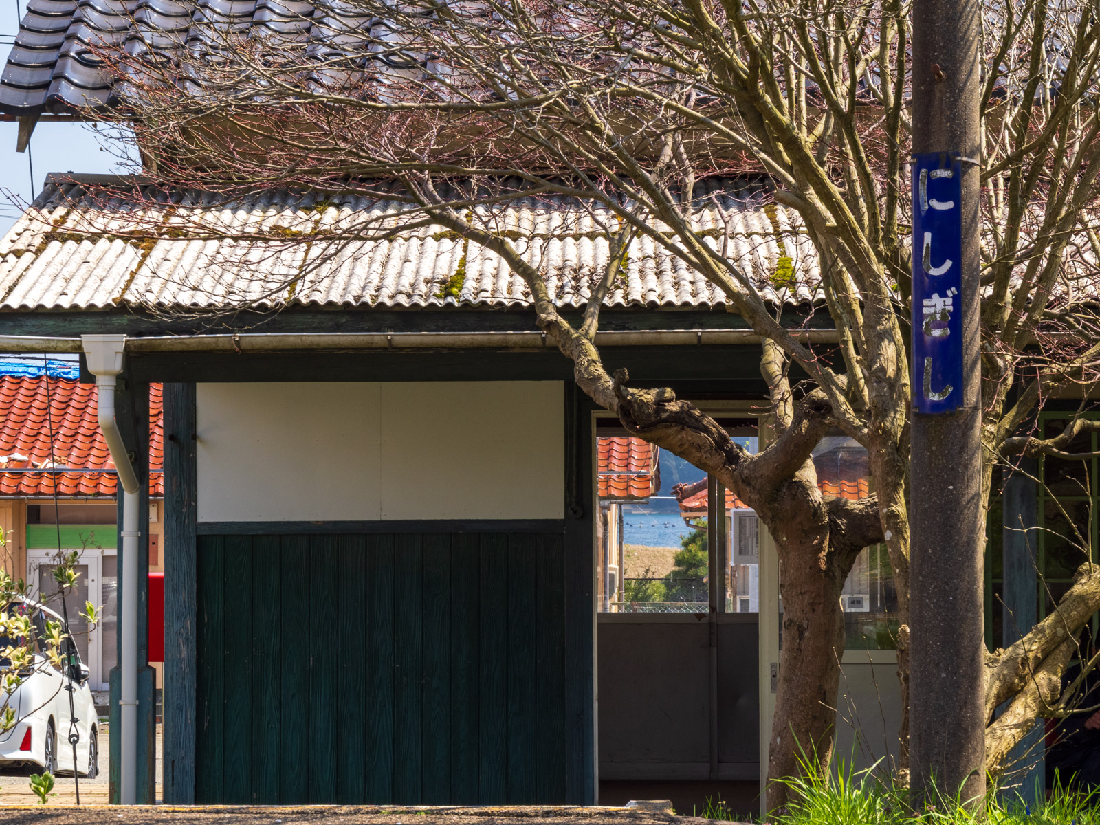 西岸駅のホーローの駅名板、駅舎と窓越しの七尾湾(2025年4月)