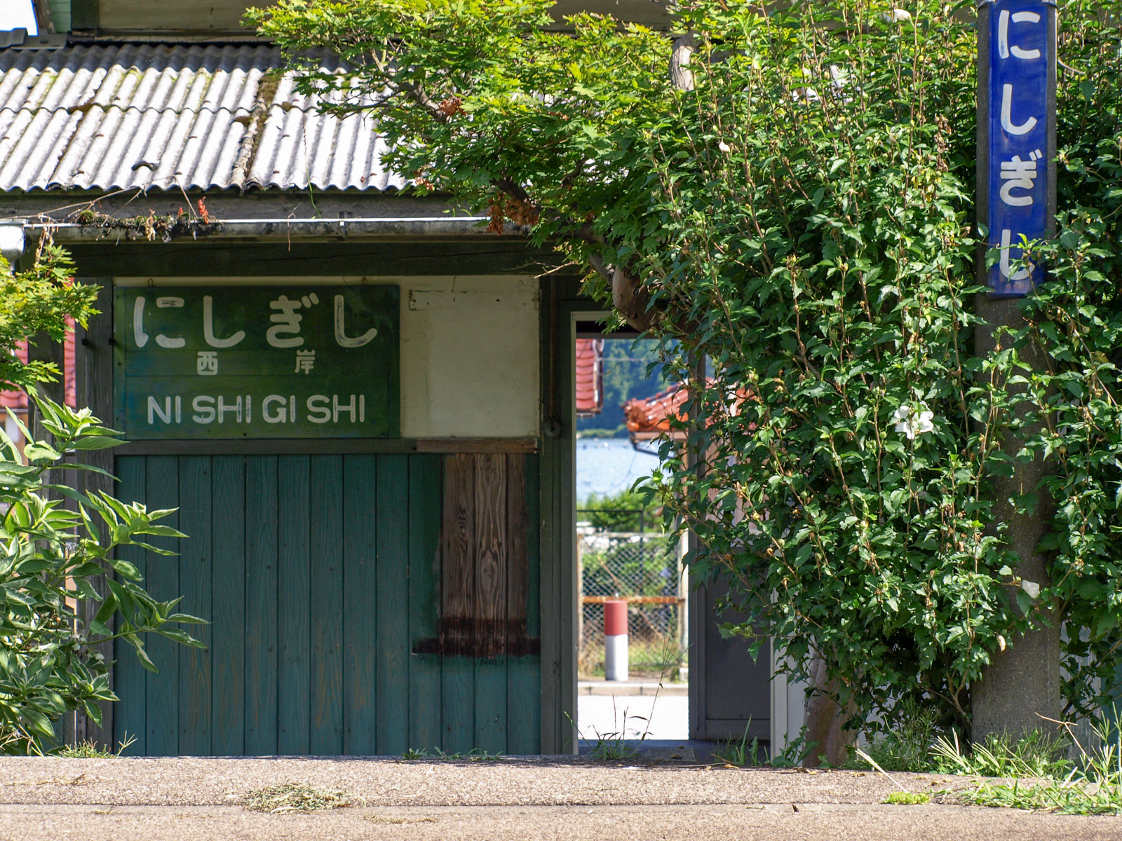 木造の駅名板が掲げられていた駅舎と、駅舎越しの七尾湾(2008年8月)
