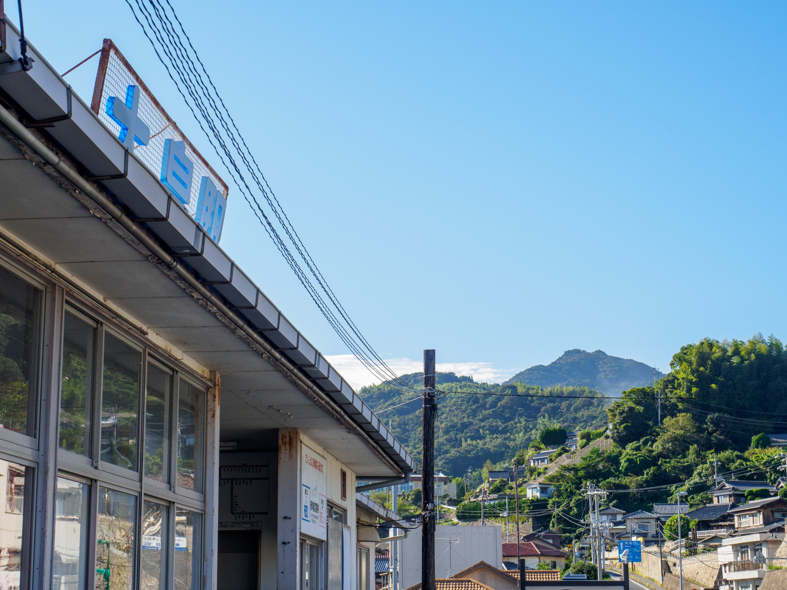 大畠駅の駅舎と、山の斜面に点在する民家（2016年10月）