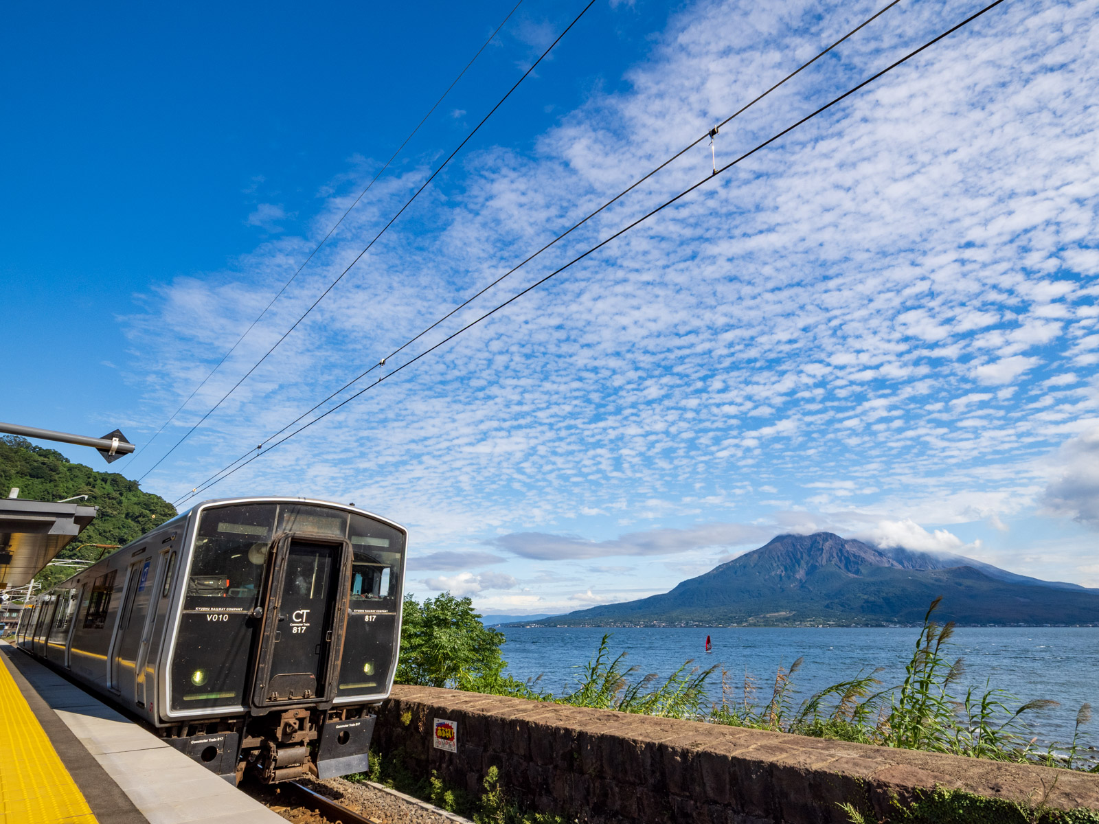 仙巌園駅に到着した列車と、錦江湾と桜島（2025年10月）