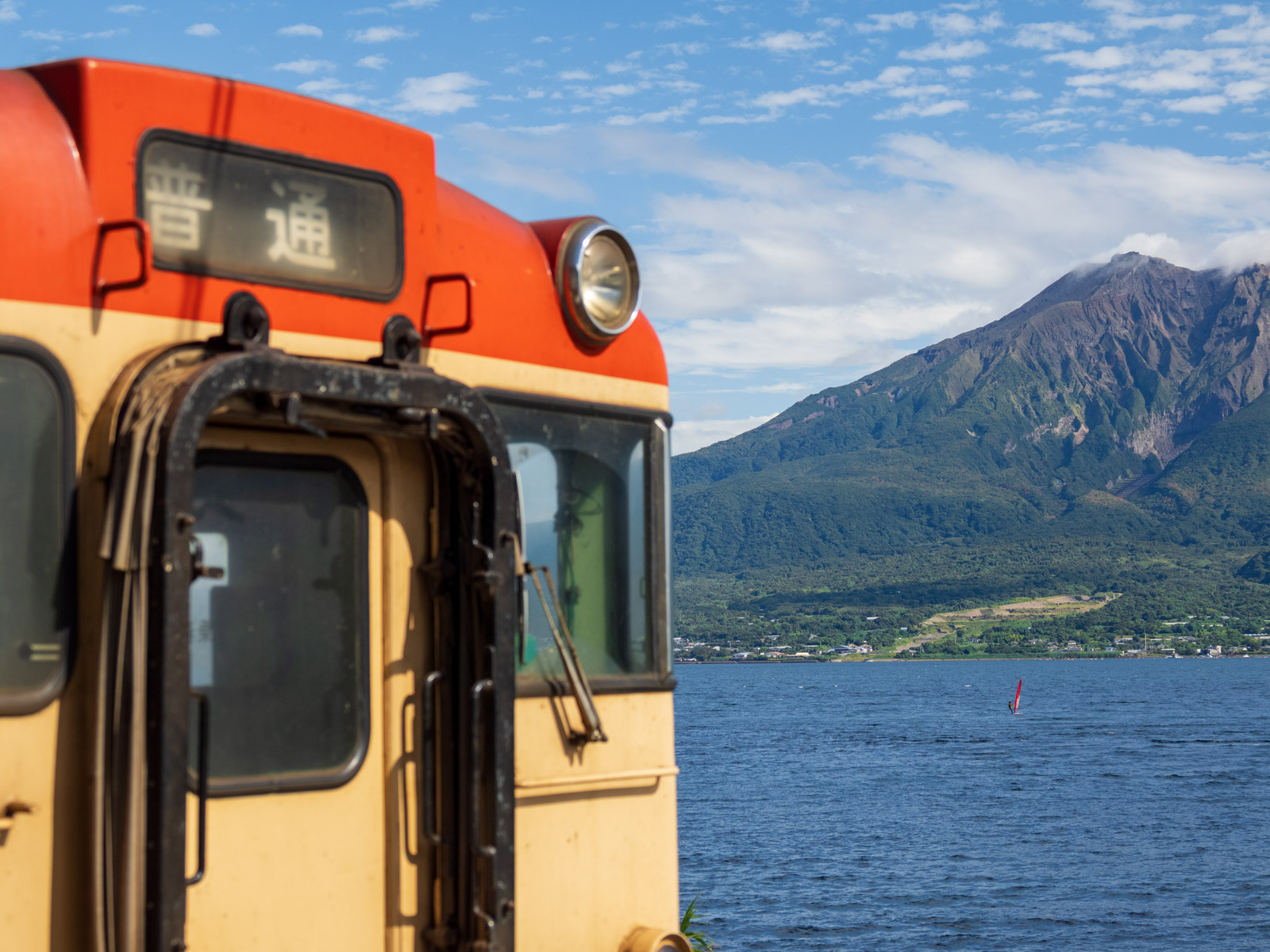 仙巌園駅に到着した列車と、錦江湾と桜島（2025年10月）