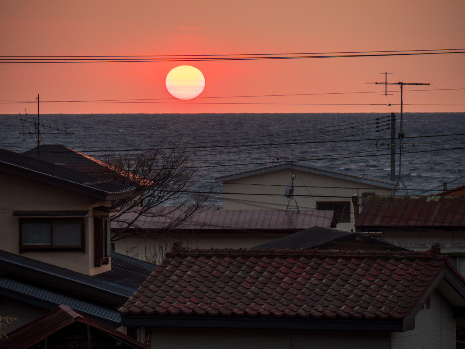 白神岳登山口駅前から見た、集落越しの日本海と夕日（2016年3月）