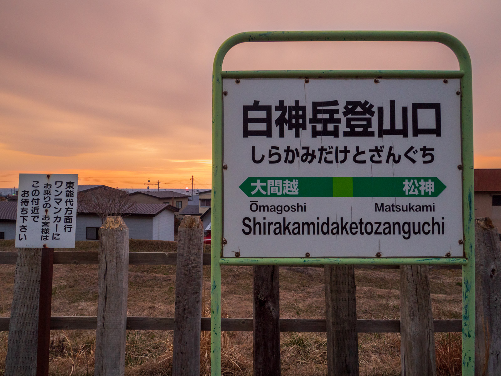 白神岳登山口駅のホームから見た、日本海に沈む夕日と駅名標（2016年3月）