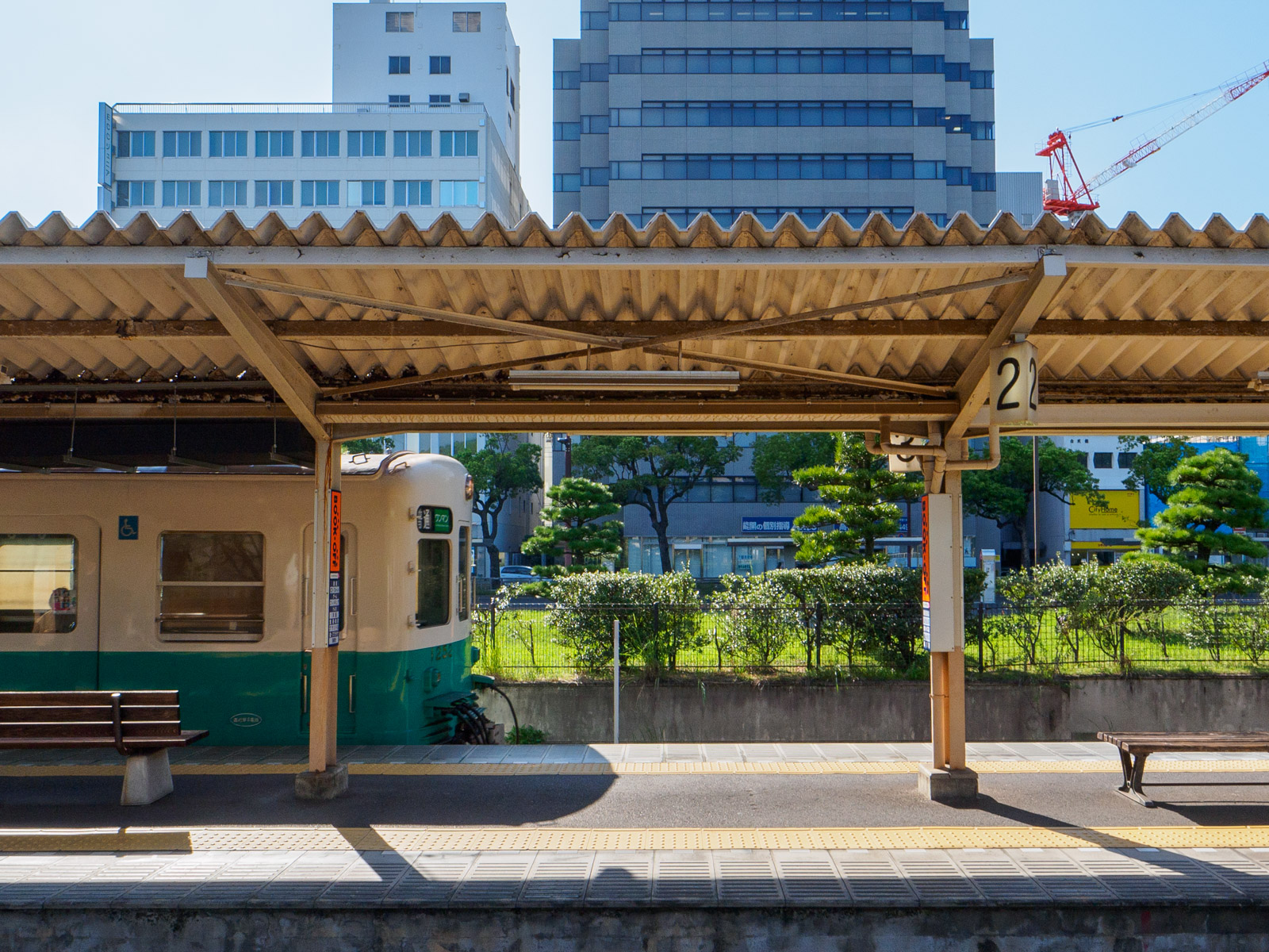 高松築港駅のホームに到着する列車と、駅前のビル群（2023年9月）