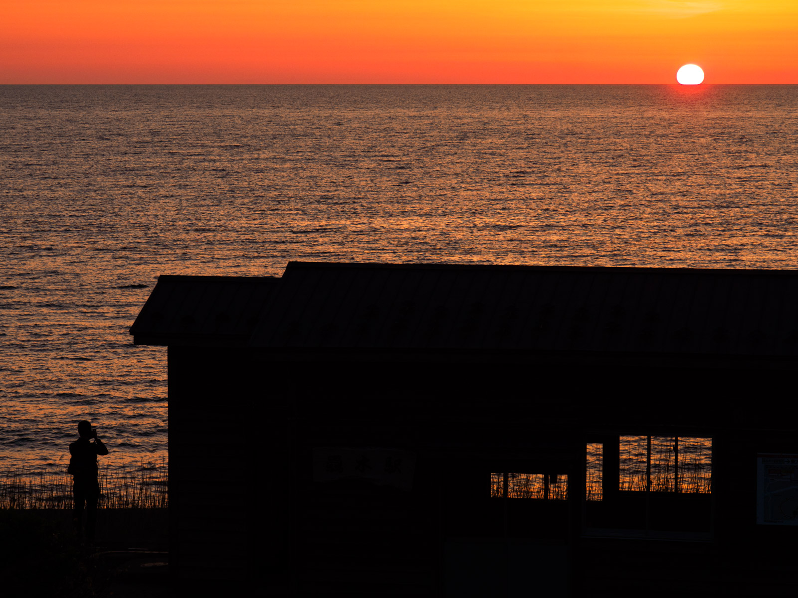 驫木駅の駅舎と、太陽が沈む日本海の水平線（2017年5月）