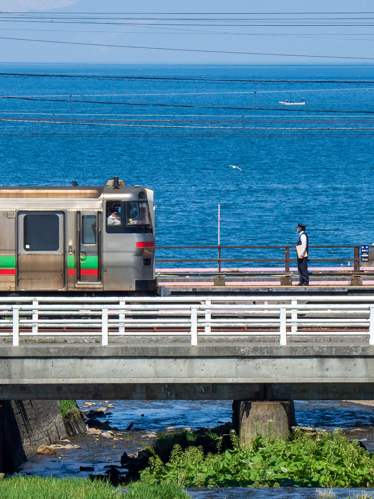 銭函川に架かる橋から見た、銭函駅に到着する列車と石狩湾（2024年5月）